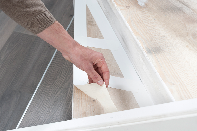 Een hand verwijdert de beschermfolie van een witte plakstrip op een houten trap.
