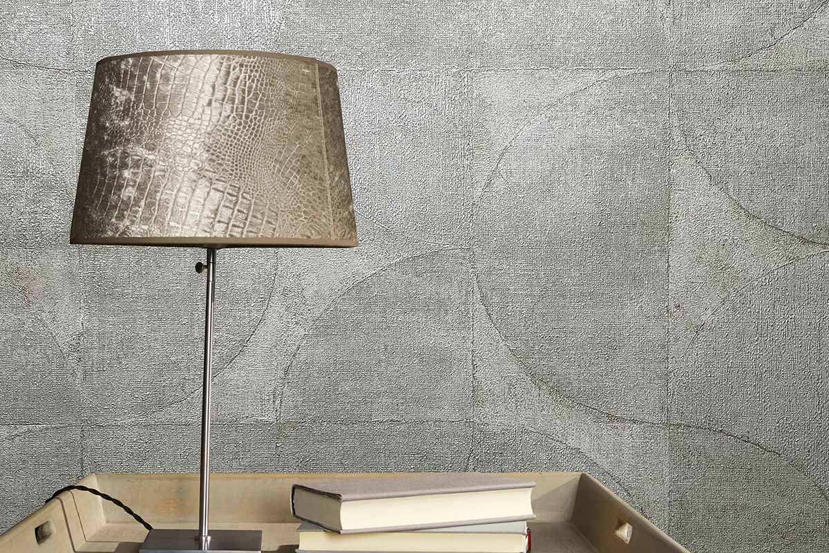 Close-up van een muur met behang, een lamp met een lampenkap met krokodillenpatroon en boeken op een nachtkastje