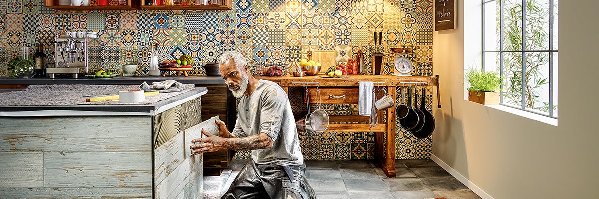 Man installeert wandpanelen in een keuken met tegels in patchworkstijl.