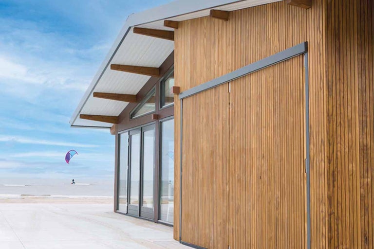 Huis met houten gevel, glazen voorkant en schuifdeur aan het strand