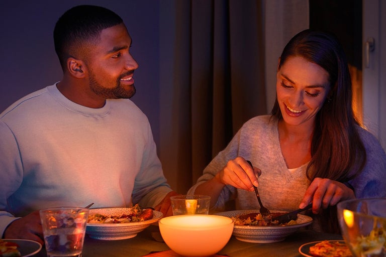 Een paar eet aan tafel, verlicht door een tafellamp.