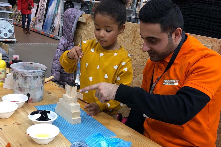 Kind en Hornbach medewerker beschilderen houten bouwstenen met penseel en verf.