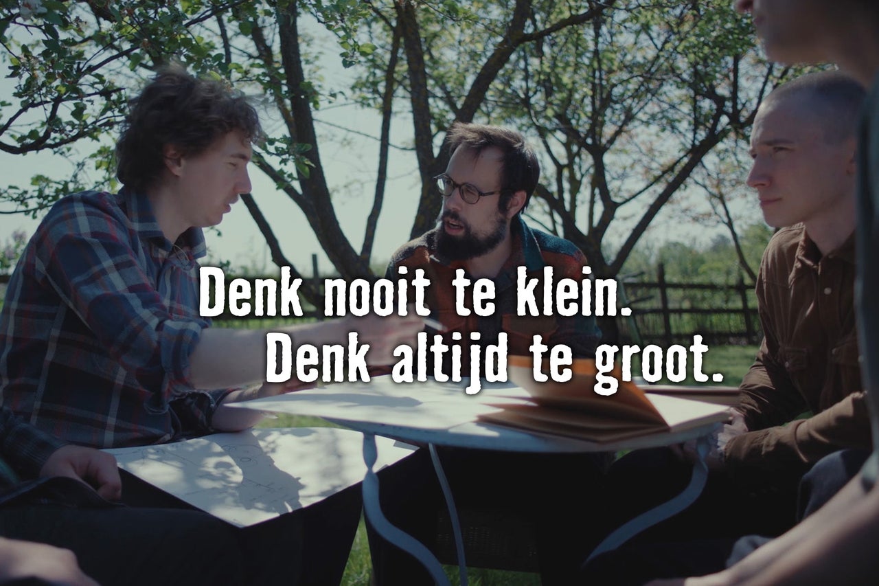 Drie mannen zitten aan een tafel in de tuin en bespreken een project aan de hand van tekeningen.