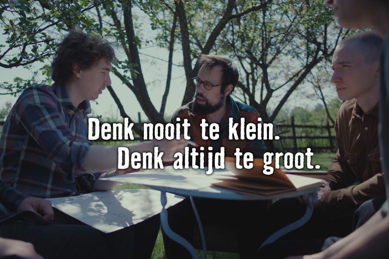 Drie mannen zitten aan een tafel in de tuin en bespreken een project aan de hand van tekeningen.