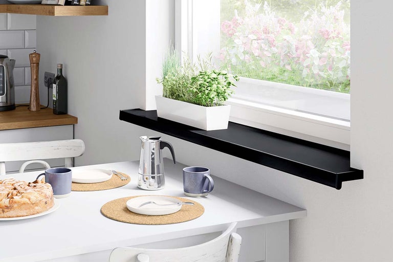 Zwarte vensterbank als smalle plank in een lichte keuken met een kruidenpot en eethoek.