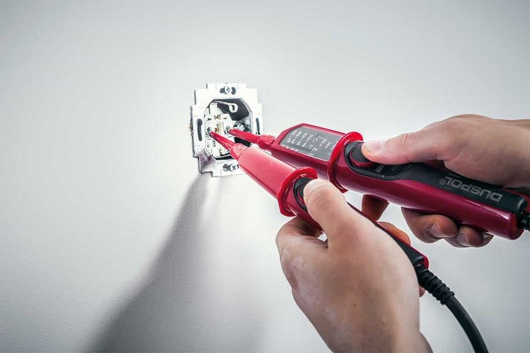 Een persoon test een stopcontact met een tweepolige spanningstester.