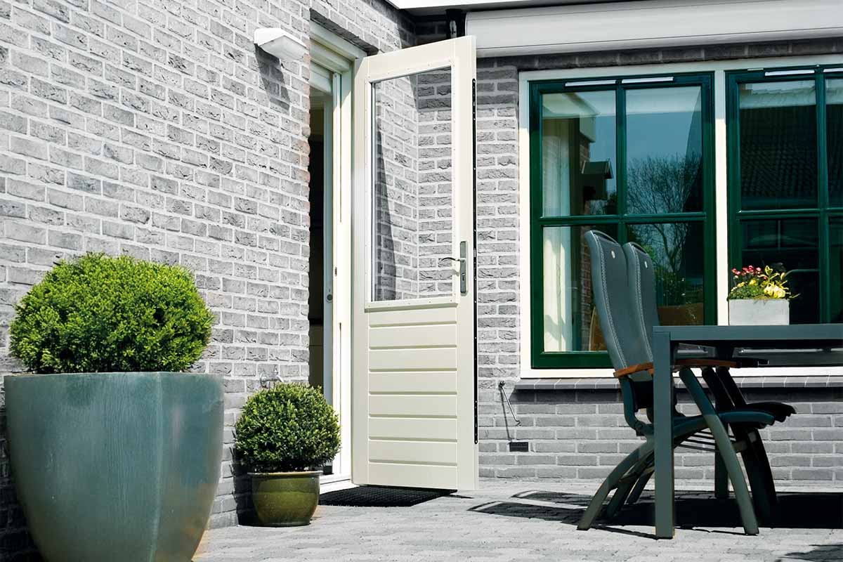 Witte achterdeur met glas en horizontale panelen in een grijze bakstenen muur op een terras met tuinmeubelen en planten.