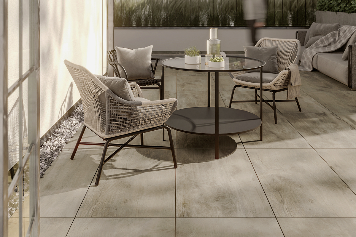 Modern terras met ronde glazen tafel, gevlochten fauteuils en lichte vloertegels in houtlook.