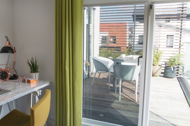 Kantoor met bureau en gordijn met toegang tot balkon met tuinmeubilair.