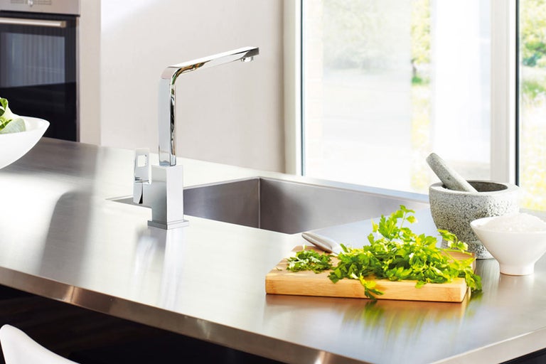 Keukenscène met spoelbak, kraan, snijplank en kruiden op een werkblad.