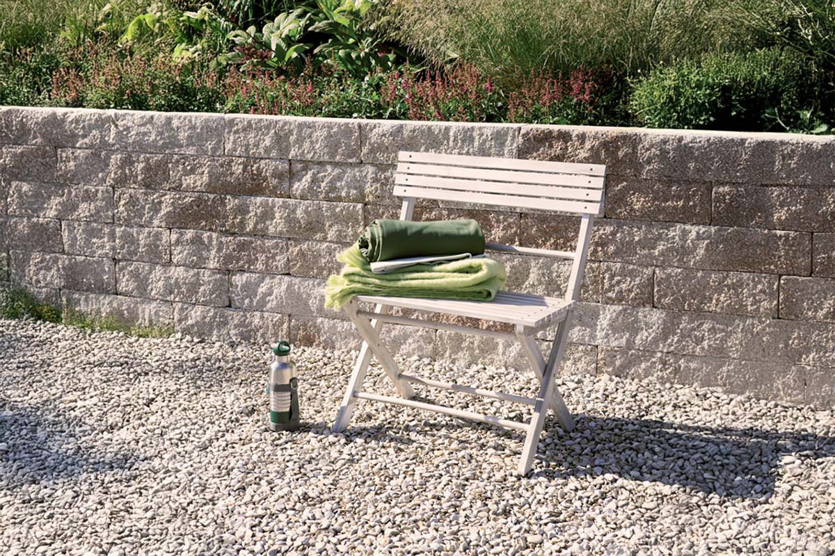 Tuinscene met steunmuur van stenen, tuinstoel, dekens en een drinkfles