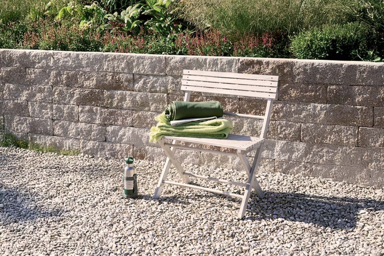 Tuinscene met steunmuur van stenen, tuinstoel, dekens en een drinkfles