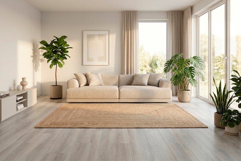 Lichte woonkamer met beige bank, groot jute vloerkleed, laminaatvloer met houtlook en kamerplanten zoals Monstera en vioolbladplant.