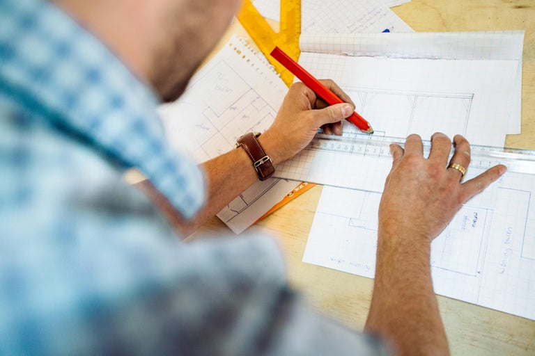 Een persoon tekent met een potlood en een liniaal op een vel papier.