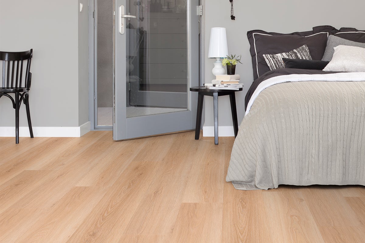 Laminaatvloer met eikenlook in een moderne slaapkamer met bed, zwarte stoel en glazen deur.