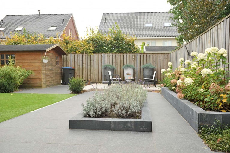 Een tuin met tuinhuis, gazon, bestrating en plantenbakken