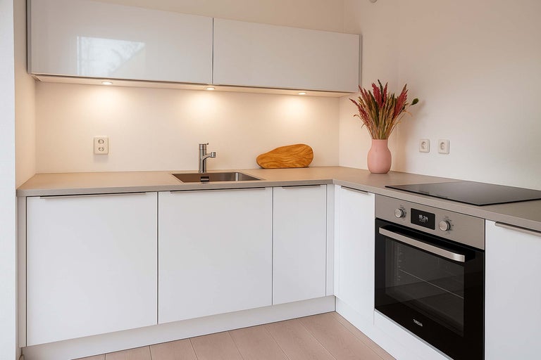 Moderne keuken met witte kasten, spoelbak en ingebouwde oven.