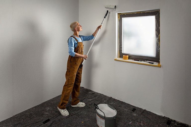 Vrouw schildert muur met verfroller in een gerenoveerde kamer.