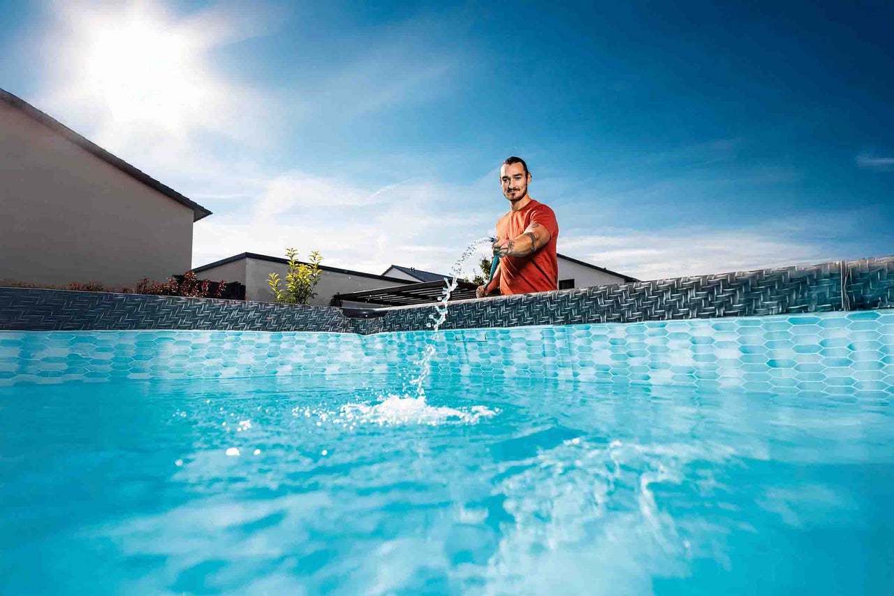 Een man vult een zwembad in de tuin met een tuinslang. Het zwembad heeft een bedrukte binnenfolie en een donkere rand.