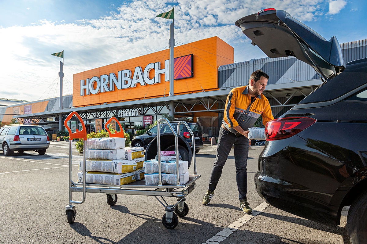 Een man laadt een winkelwagen met bouwmaterialen in voor een Hornbach-winkel.