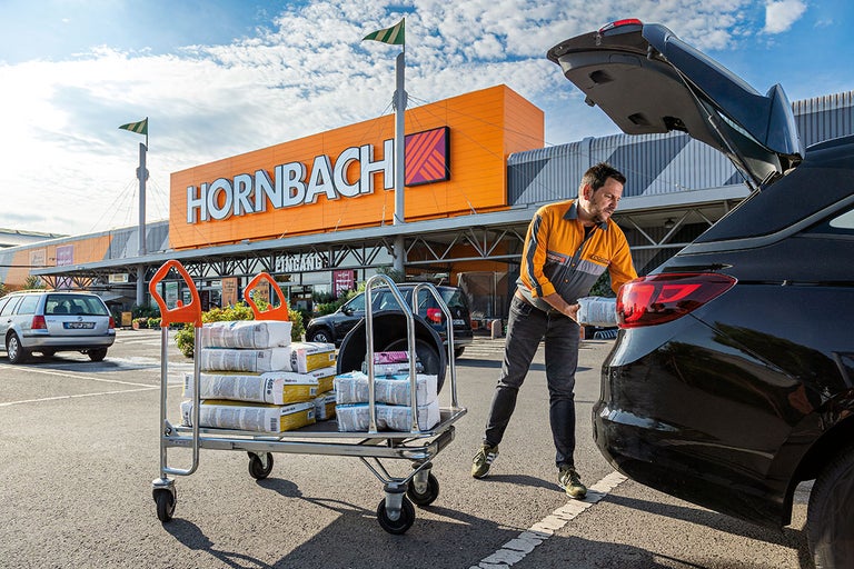 Een man laadt een winkelwagen met bouwmaterialen in voor een Hornbach-winkel.