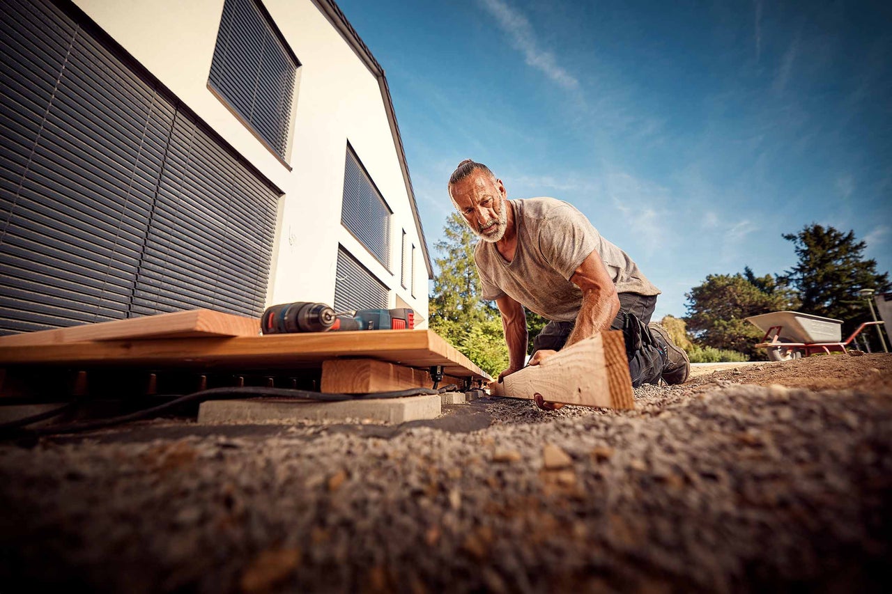 Man legt een houten terras aan in de tuin van een woonhuis.