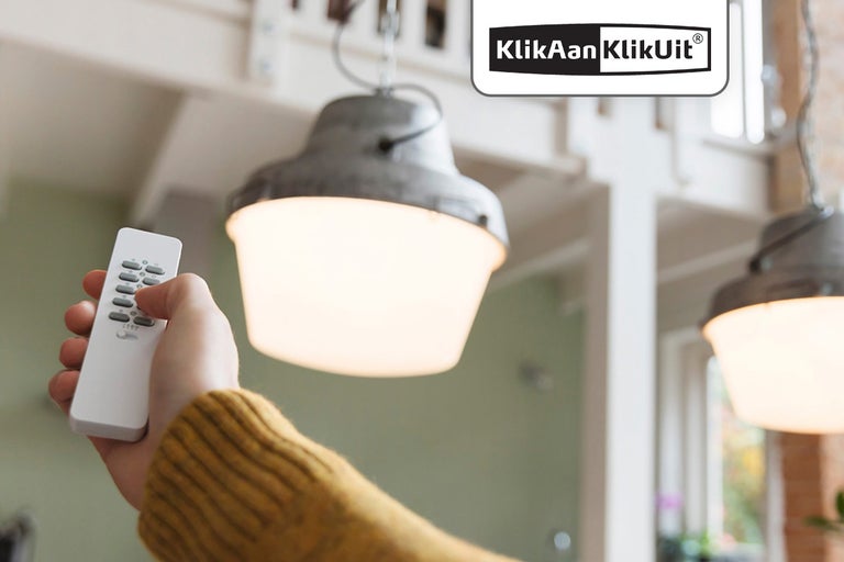 Persoon bedient lamp met KlickAan KlikUit afstandsbediening, KlickAan KlikUit logo