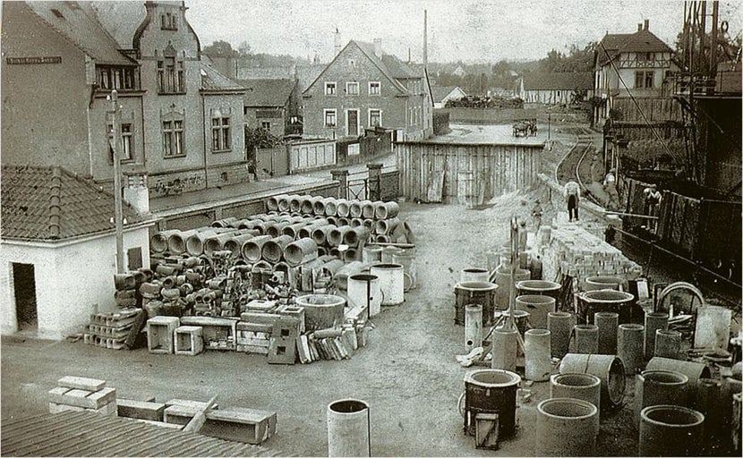 Historische afbeelding van een opslagplaats met buizen en bouwmaterialen in een fabriekscomplex