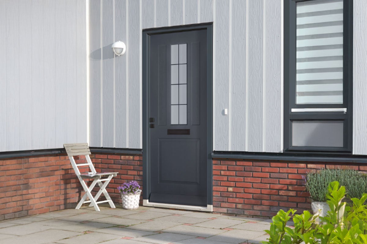 Moderne gevel met antracietkleurige voordeur met glaselement, witte wandpanelen en rode bakstenen op een terras met een witte klapstoel.
