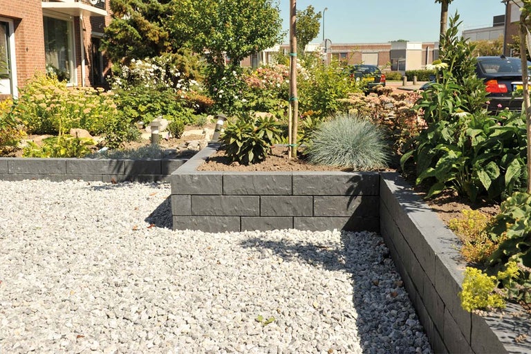 Tuinscene met beplante verhoogde bedden van betonblokken en een grindpad