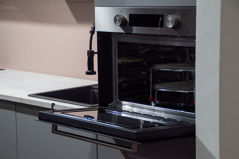 Inbouwoven met geopende glazen deur van roestvrij staal in een moderne keuken naast een gootsteen.