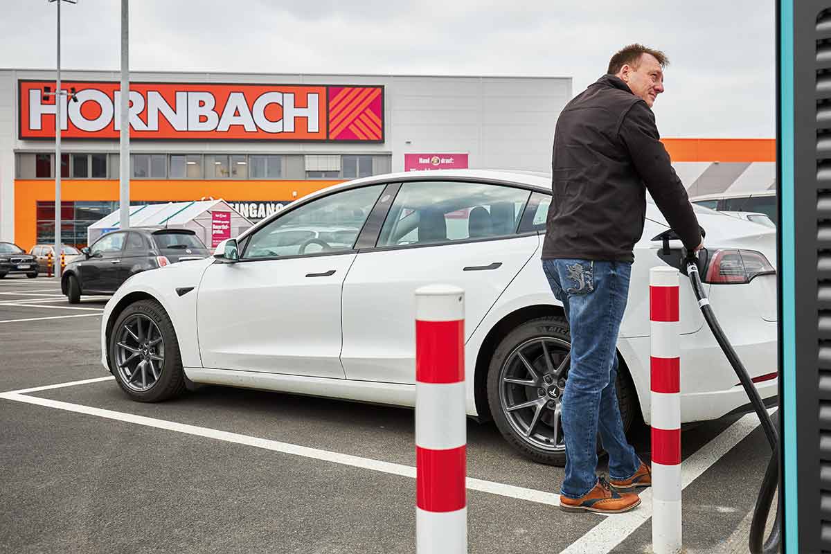 Man laadt een witte elektrische auto op de parkeerplaats voor een Hornbach-winkel