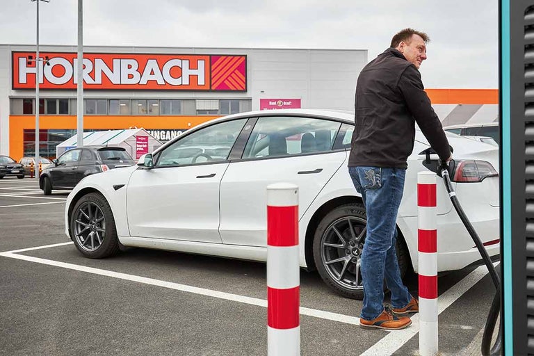 Man laadt een witte elektrische auto op de parkeerplaats voor een Hornbach-winkel
