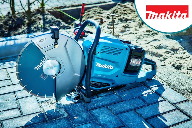 Makita doorslijpmachine met doorslijpschijf op straatstenen, zand en bouwmarkeringen op de achtergrond. Makita logo.