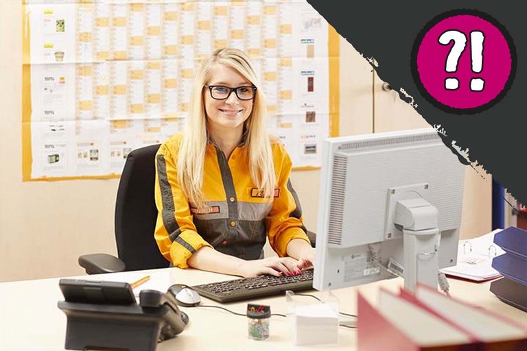 Een medewerkster zit aan een bureau met een computer en telefoon.