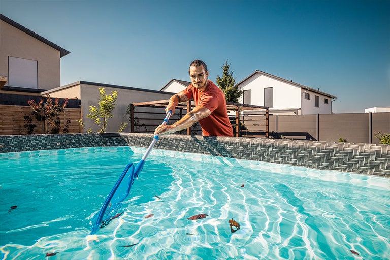 Man maakt zwembad schoon met zwembadschepnet in de tuin.