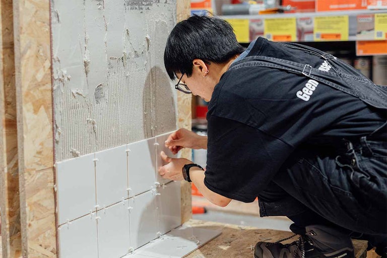 Een tegelzetter plaatst witte tegels op een muur.