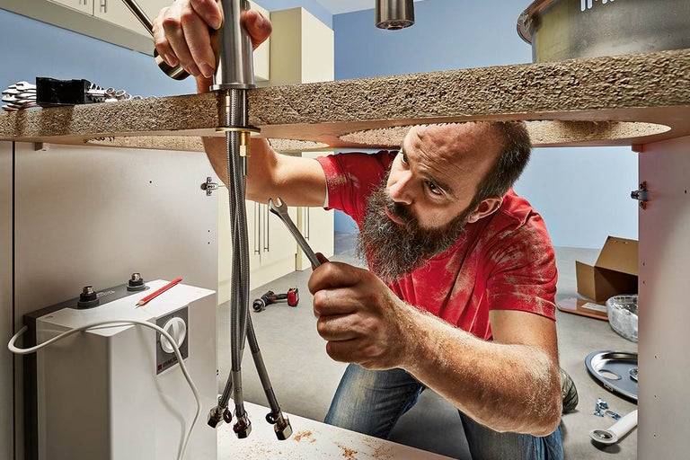 Een loodgieter installeert een kraan in een badkamer.