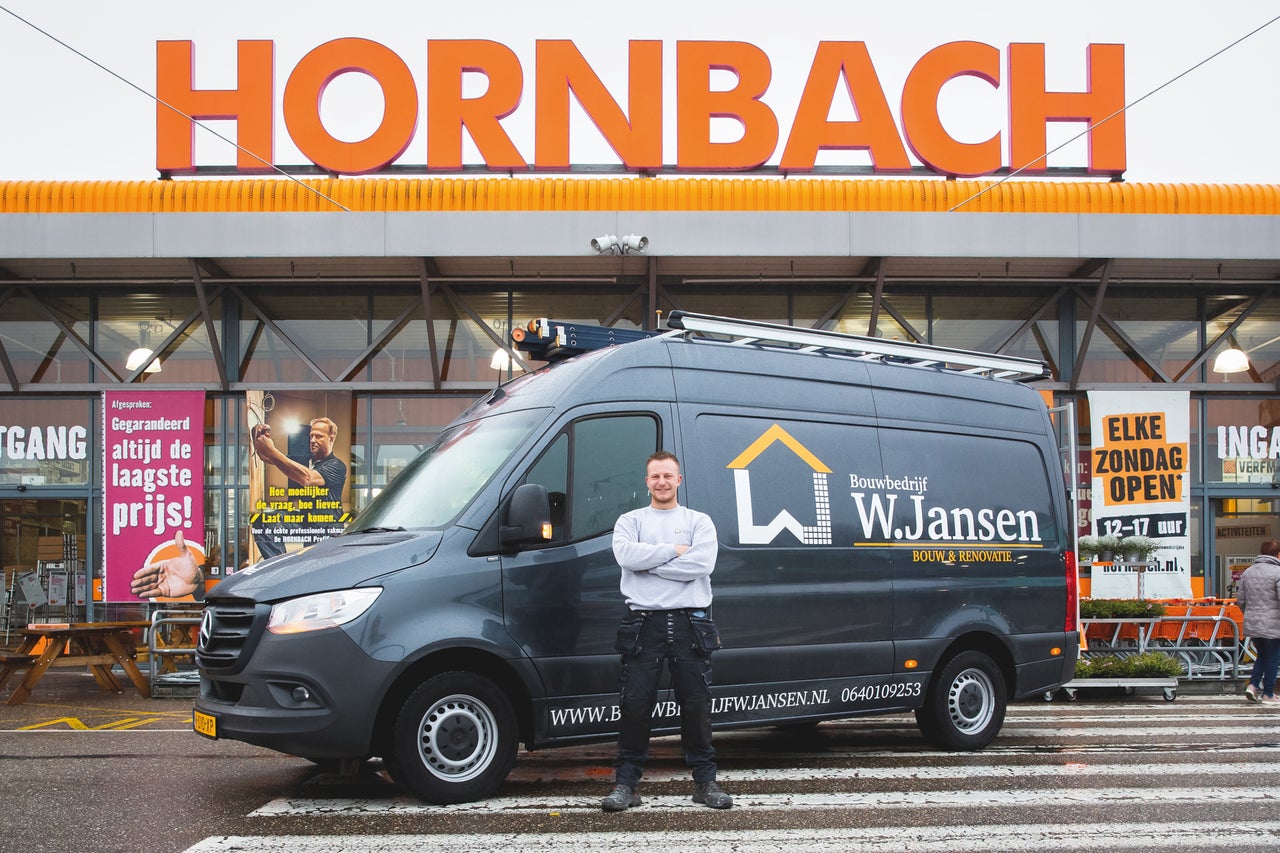 Ambachtsman voor een donkergrijze bedrijfswagen met bedrijfslogo en Hornbach filiaal