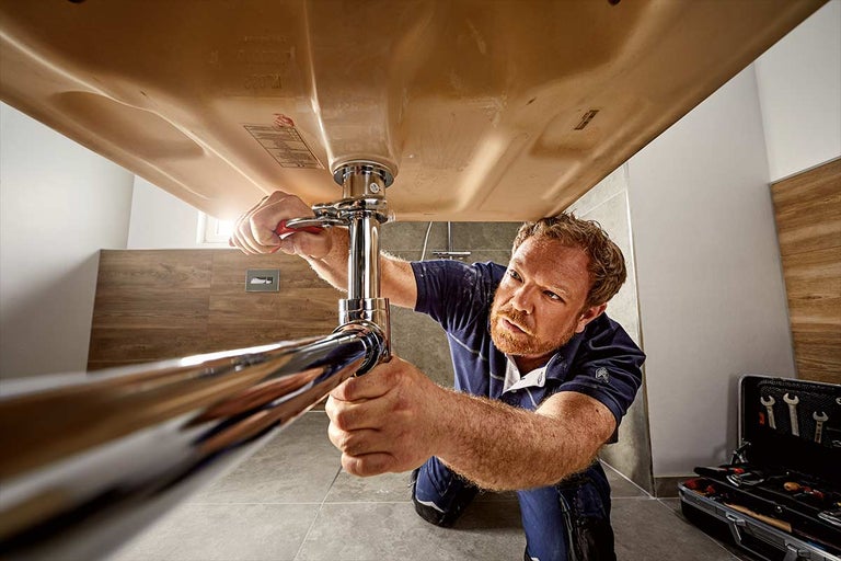 Een loodgieter repareert een wastafel in de badkamer met een pijpsleutel.