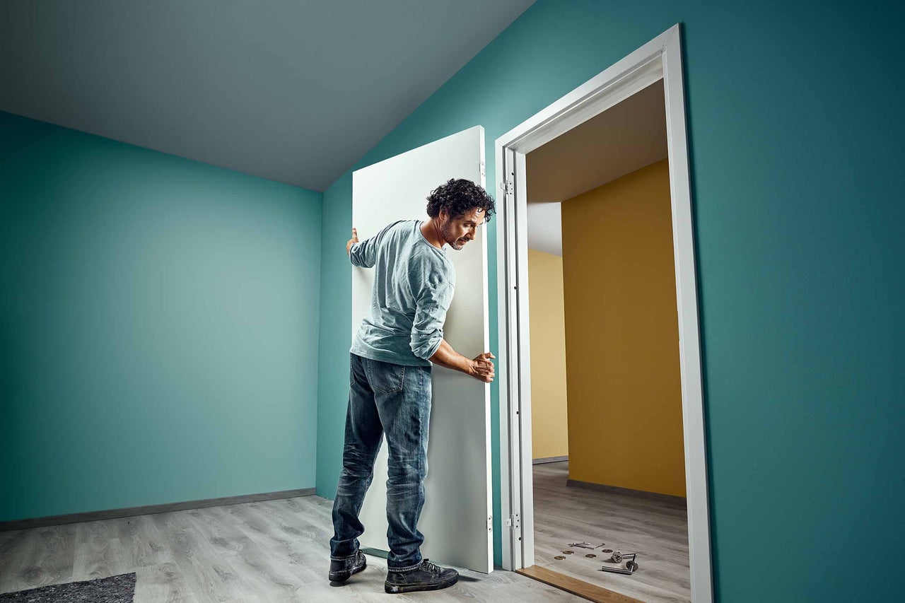 Man installeert een witte binnendeur in een gerenoveerde kamer