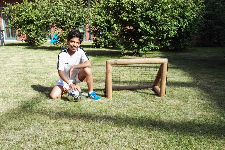 Jongen knielt op het gazon met een voetbal naast het voetbaldoel