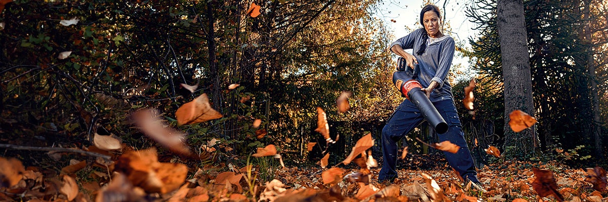 Vrouw gebruikt bladblazer in de tuin om herfstbladeren te verwijderen.