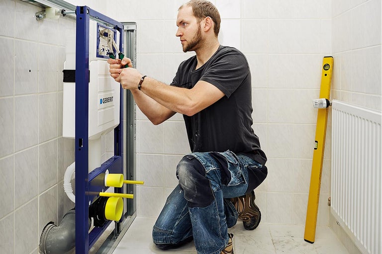 Een installateur monteert een Geberit inbouwreservoir in de badkamer met gereedschap.