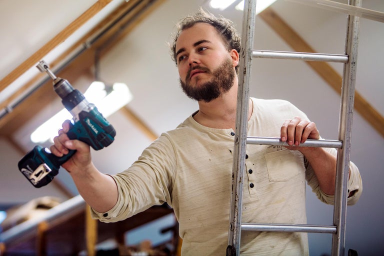 Een man staat op een ladder en houdt een accuschroefboormachine vast.