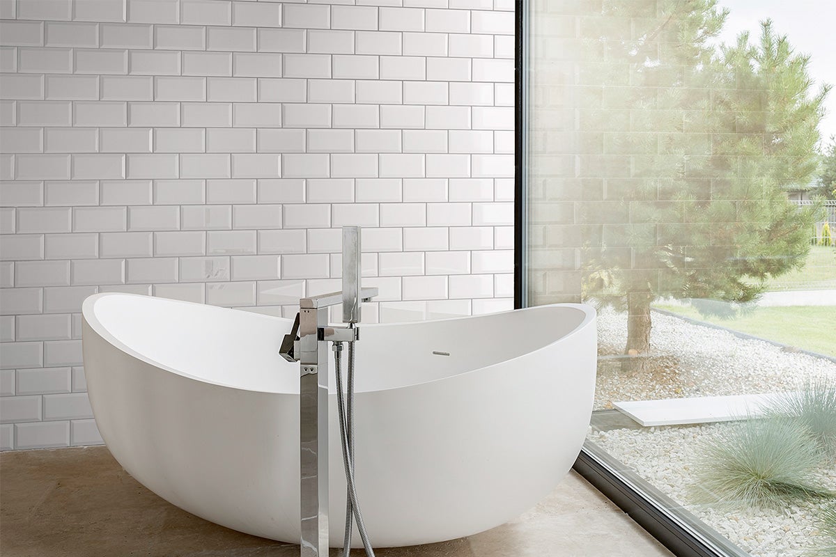 Vrijstaand bad in badkamer met witte metrotegels en raam
