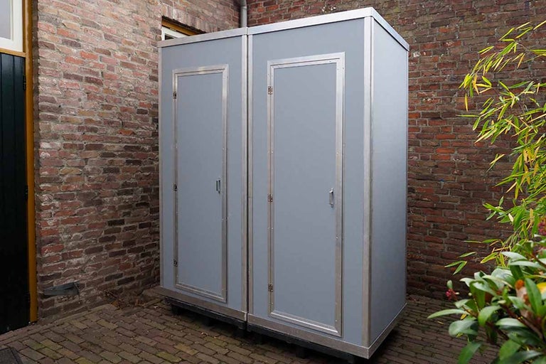 Twee grijze toiletcabines staan buiten.