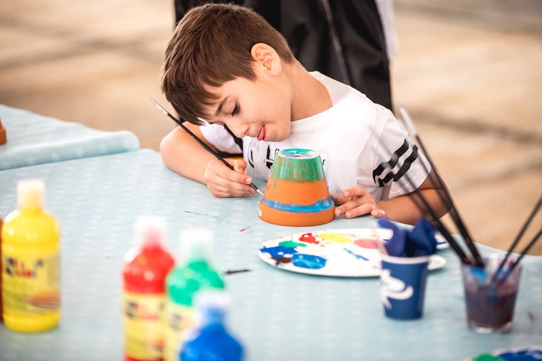 Jonge jongen schildert een bloempot met verf en een penseel op een tafel.