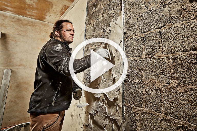 Een man brengt gips aan op een bakstenen muur