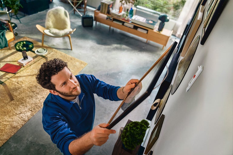 Man hangt fotolijsten met ophangsysteem aan de muur in de woonkamer.